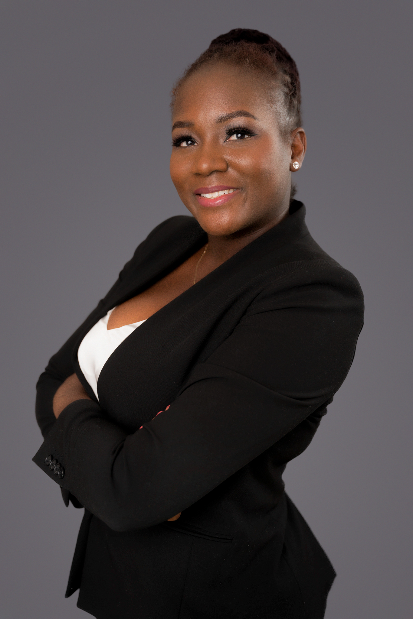 Portrait of Raychelle Fowler, author and speaker, smiling confidently in a black blazer and white top against a neutral grey background.